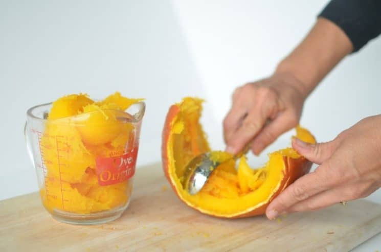 someone scooping pumpkin from it's shell into a glass container.